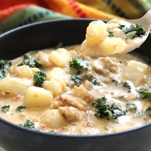 Image of vegan and gluten free creamy potato sausage kale soup in a bowl with a spoon.