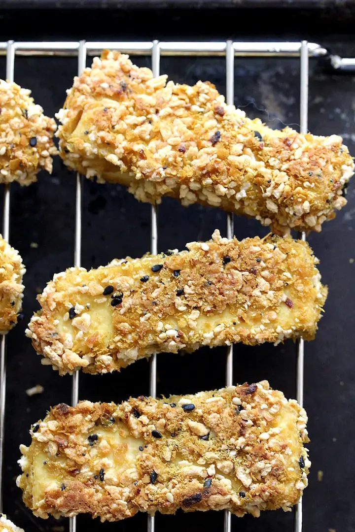 A vertical image of 3 everything bagel tofu strips on a cooling rack places on a cookie sheet.