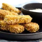 horizontal image of everything bagel tofu strips on a black circular plate with a small black bowl filled with vegan cream cheese scallion dip ion the plate in the background