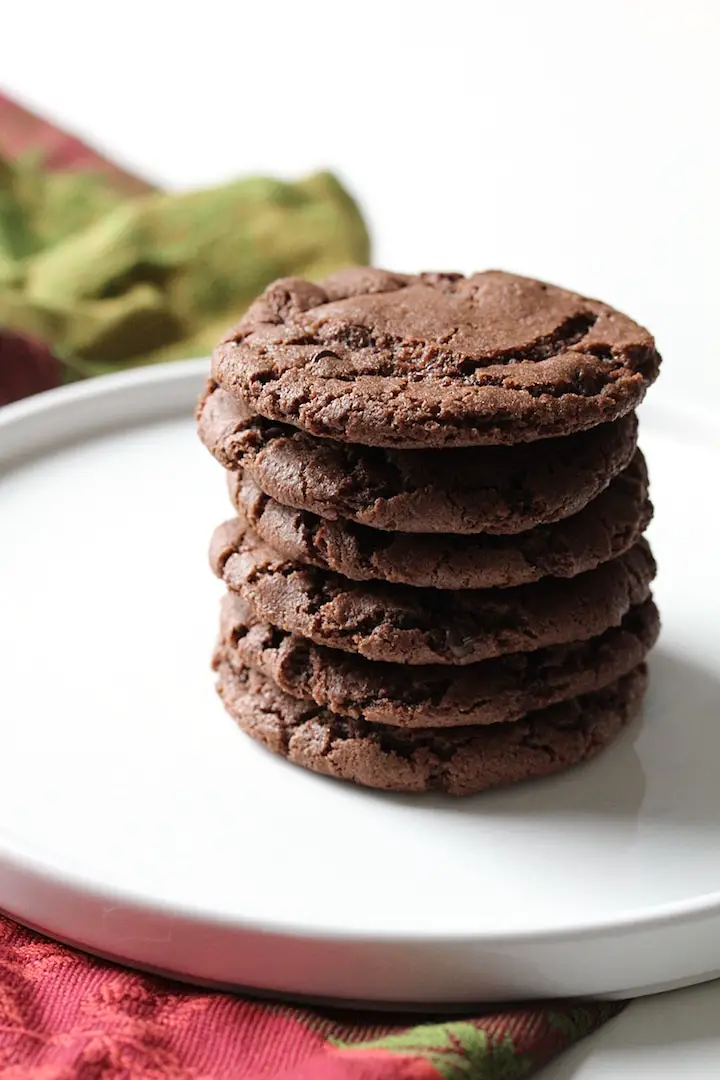 image of Chewy Chocolate Raspberry Cookies stacked on a white plate with a tea towel in the background