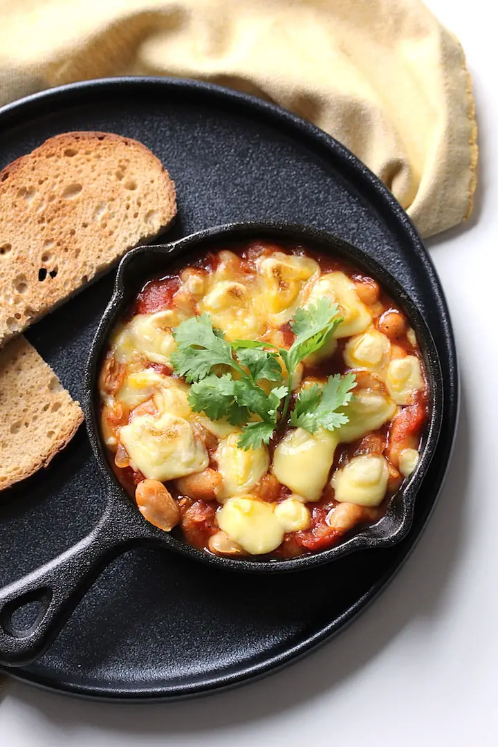 Image of easy vegan pantry shakshuka in a mini cast iron pan on a black plate with gluten-free toast