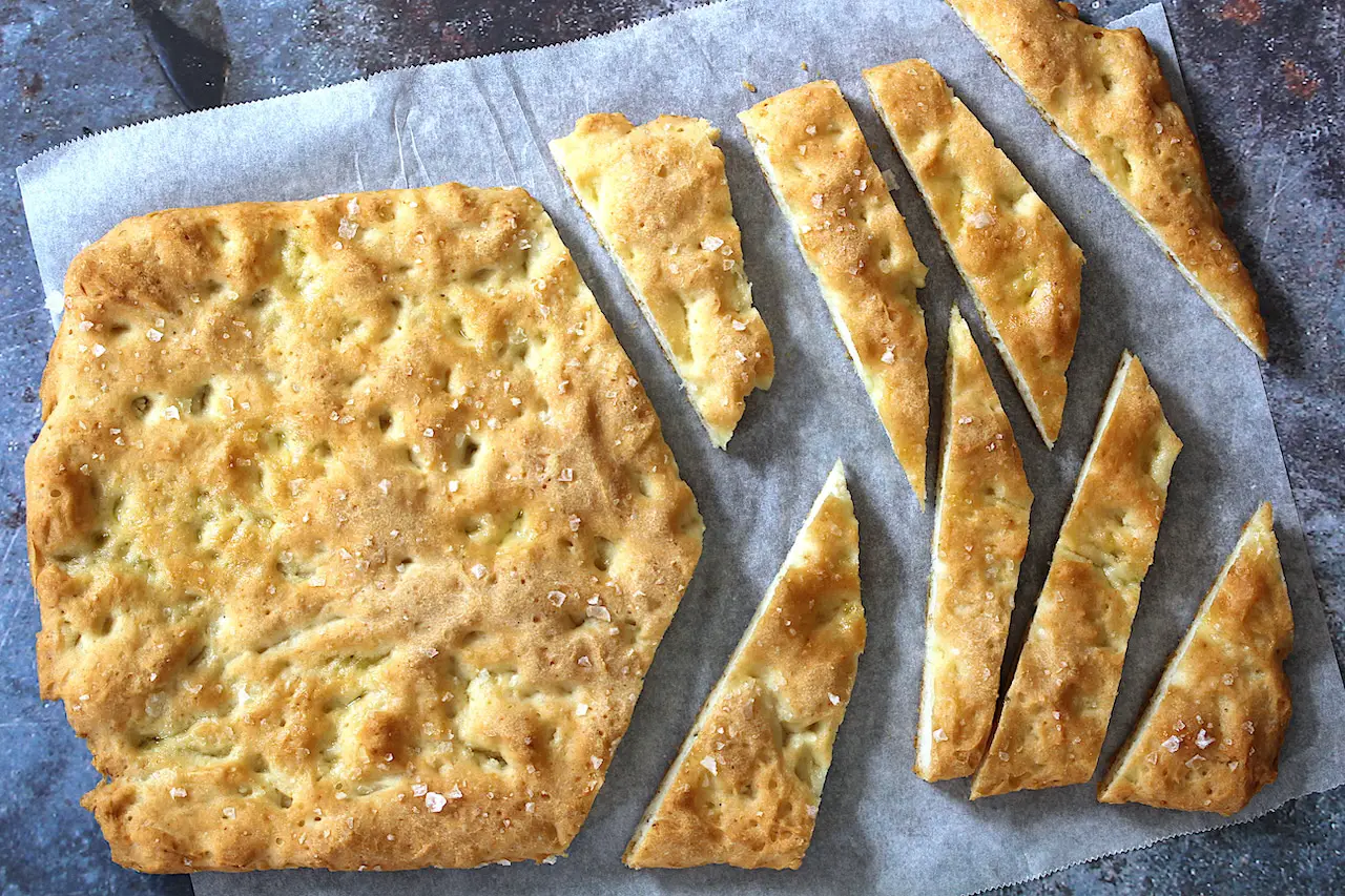 image of the delicious gluten-free vegan focaccia bread recipe. Some of the bread is sliced into strips and on parchment paper.