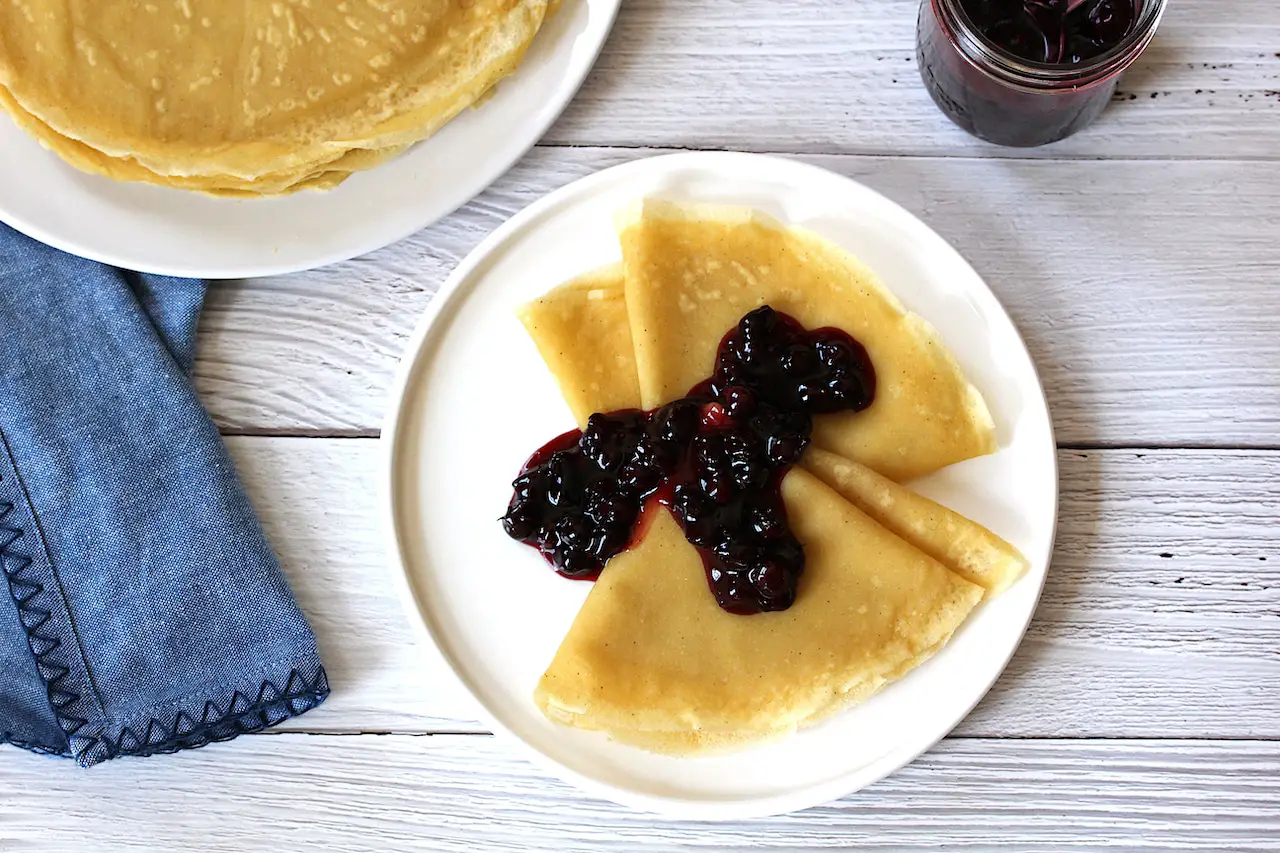  image of gluten free vegan crepes on a white plate topped with saskatoon berry sauce