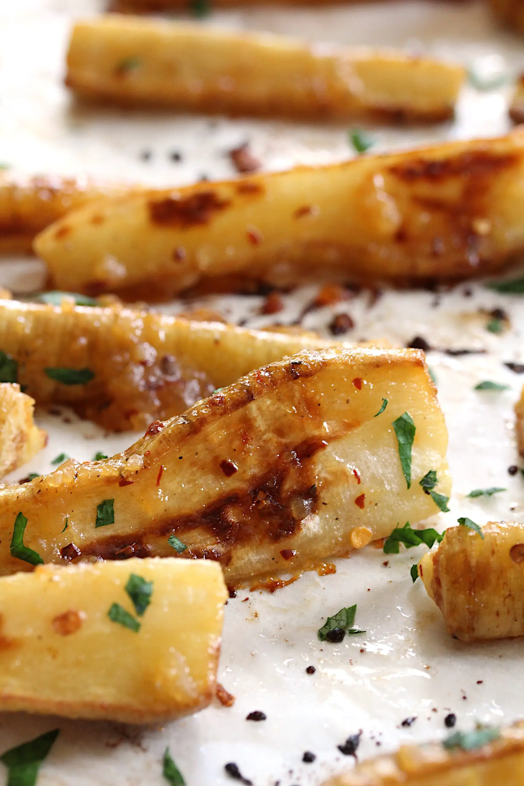 Close up image of roasted miso maple glazed parsnips on a baking sheet lined with parchment paper