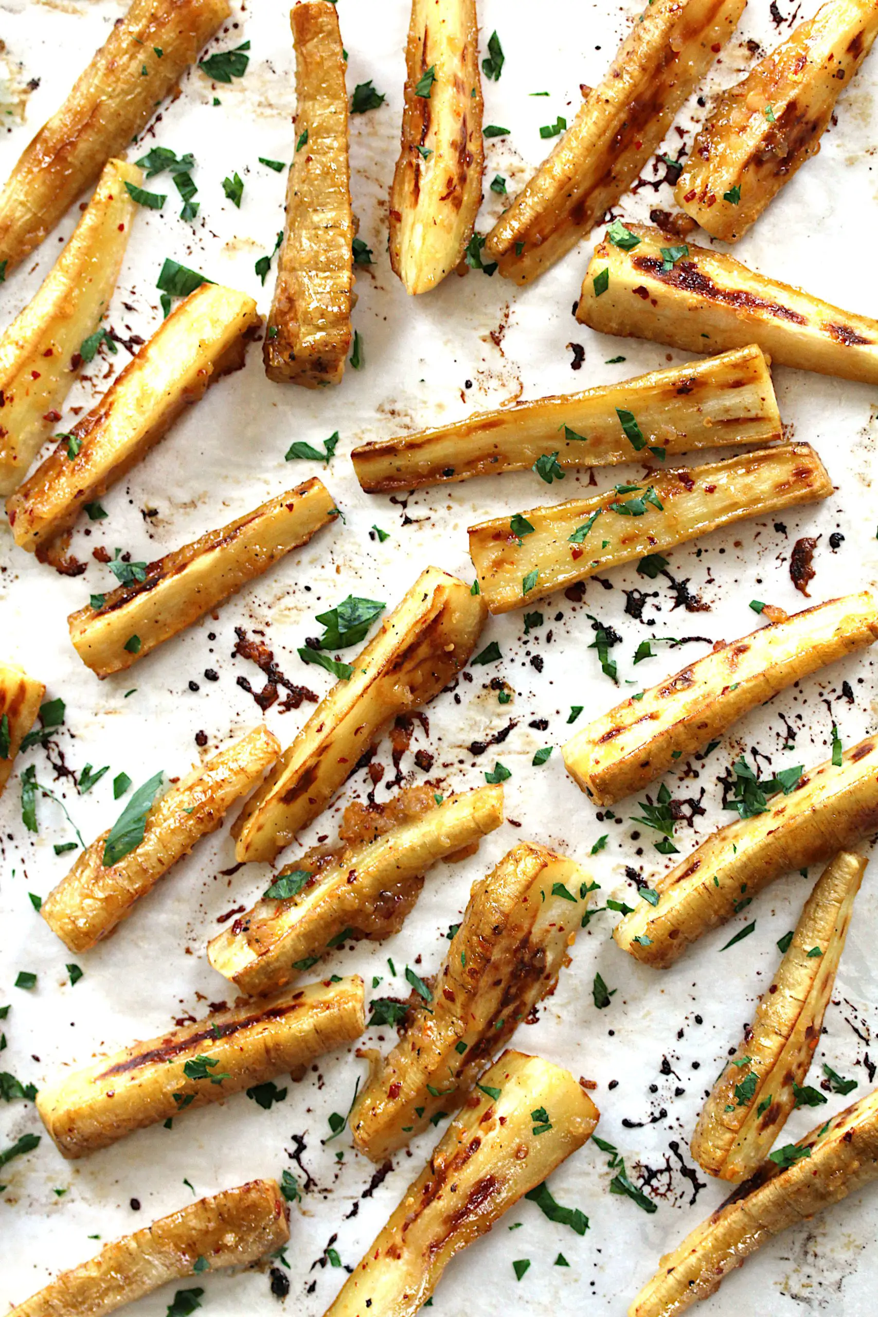 Overhead image of roasted parsnips that are spread out on a baking sheet lined with parchment paper