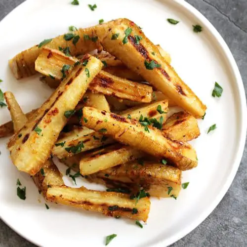 Square image of roasted parsnips on a white plate.