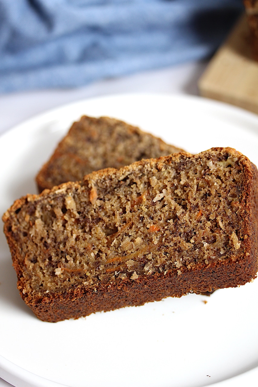 Two slices of Coconut Carrot Banana Bread on a white plate with a blue napkin in the background